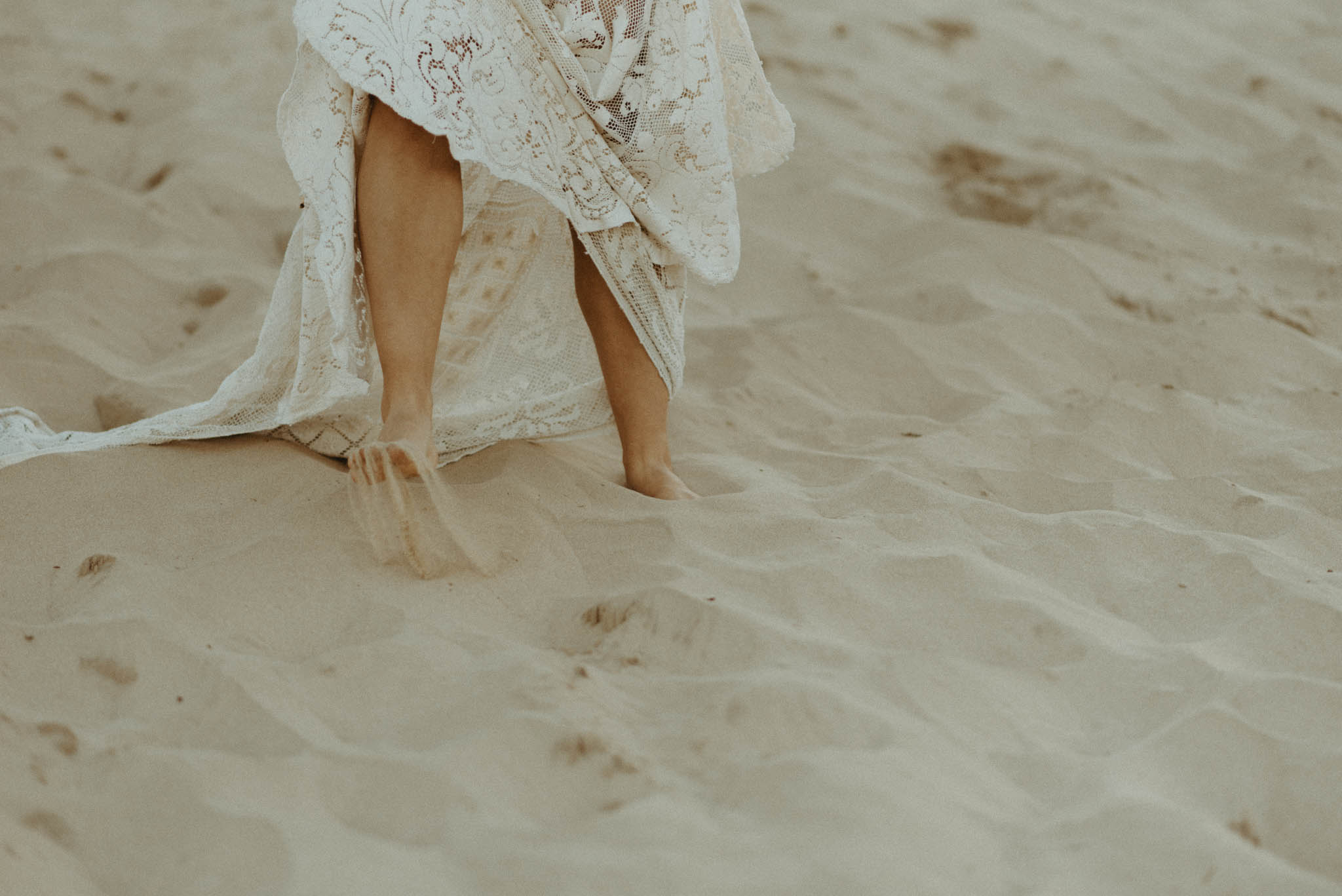 bride in lace dress walking barefoot in the sand