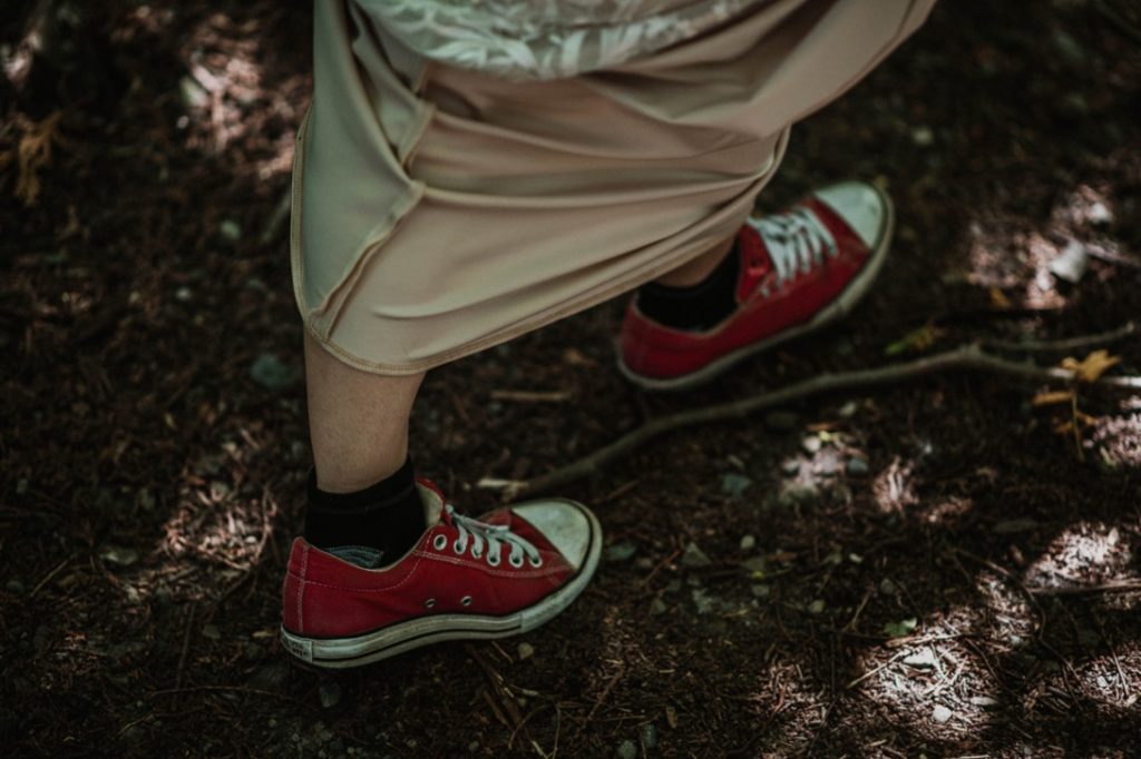 bride in white wedding dress walks through forest in red canvas sneakers