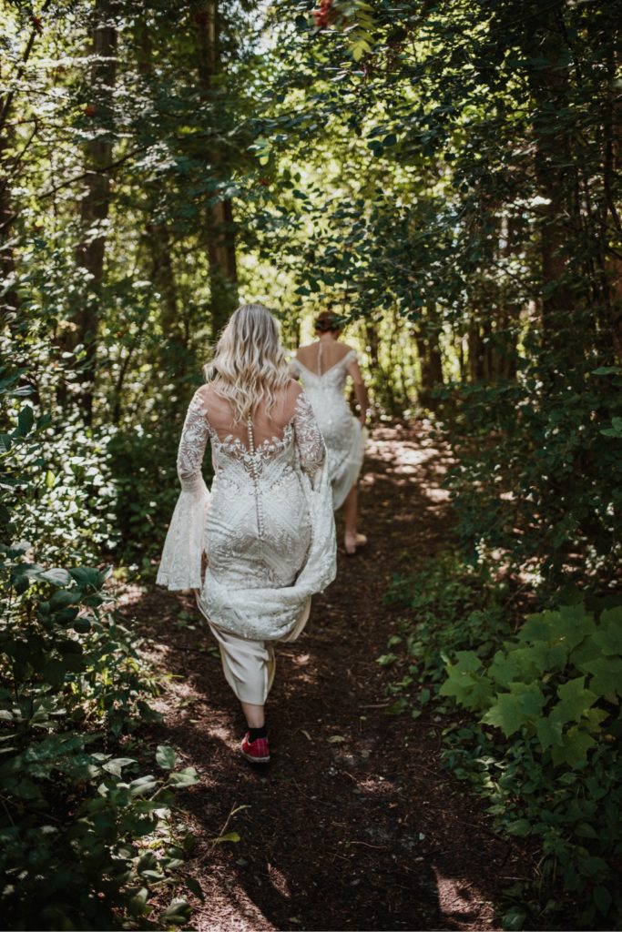 two brides in wedding dresses walk through forest