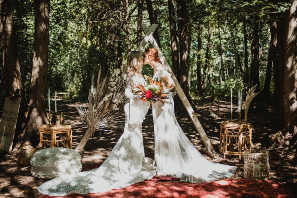lesbian couple in front of wooden triangle arch at forest ceremony