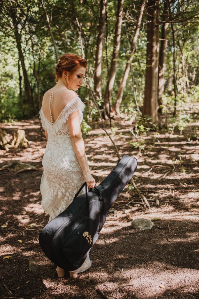 bride carrying guitar through forest trail