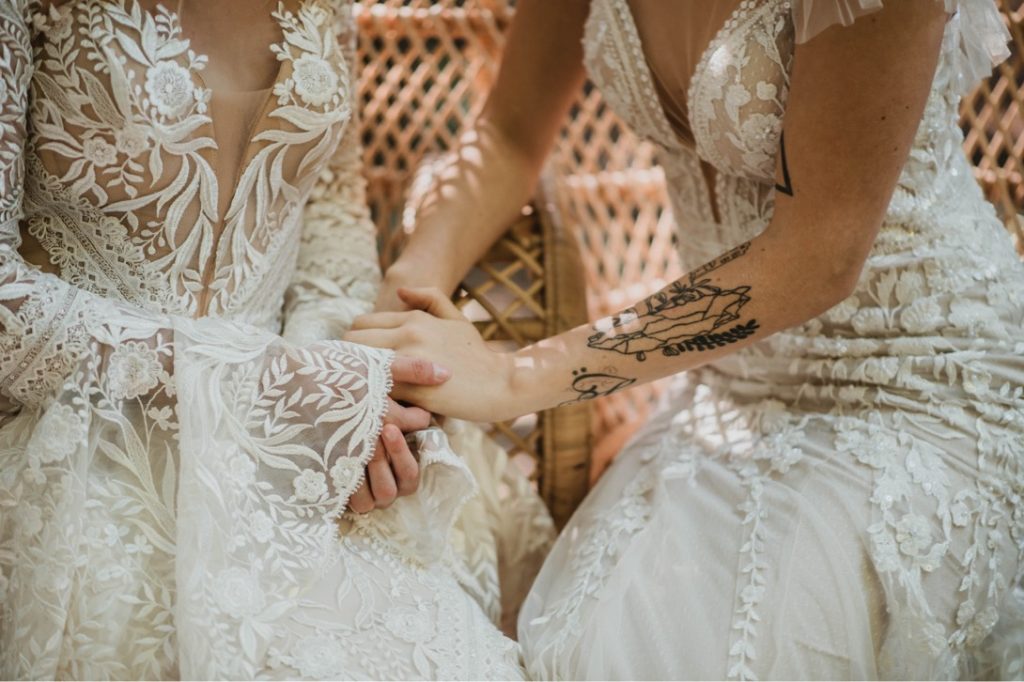 two brides in wedding dresses holding hands