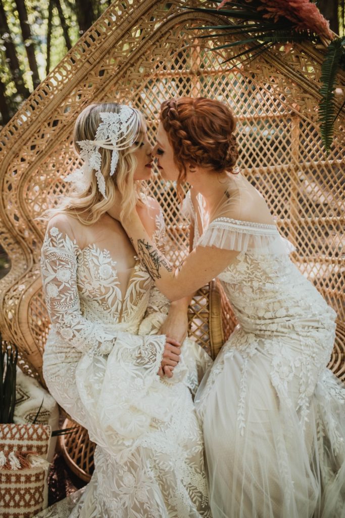 two brides kissing sit in rattan peacock chair 