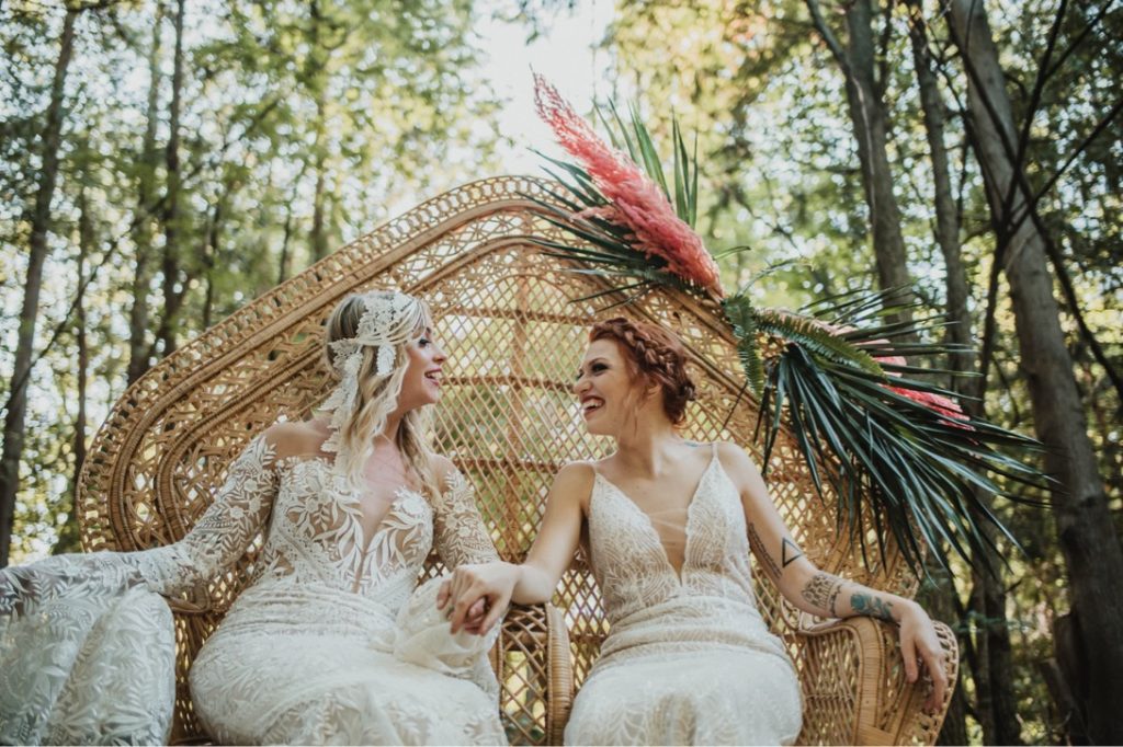 lesbian brides laughing while sitting in rattan peacock chair