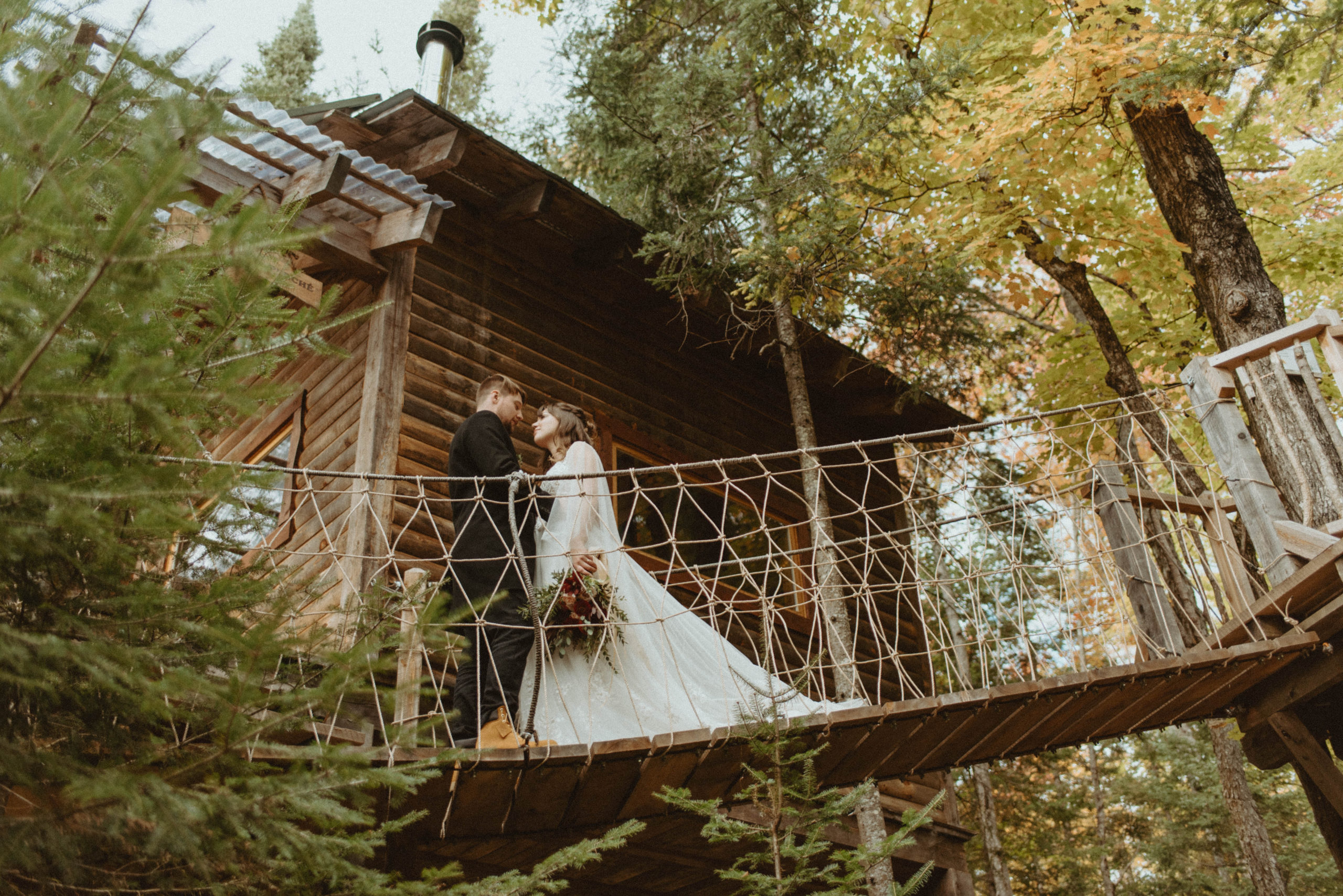bride and groom on treehouse rope ladder in forest