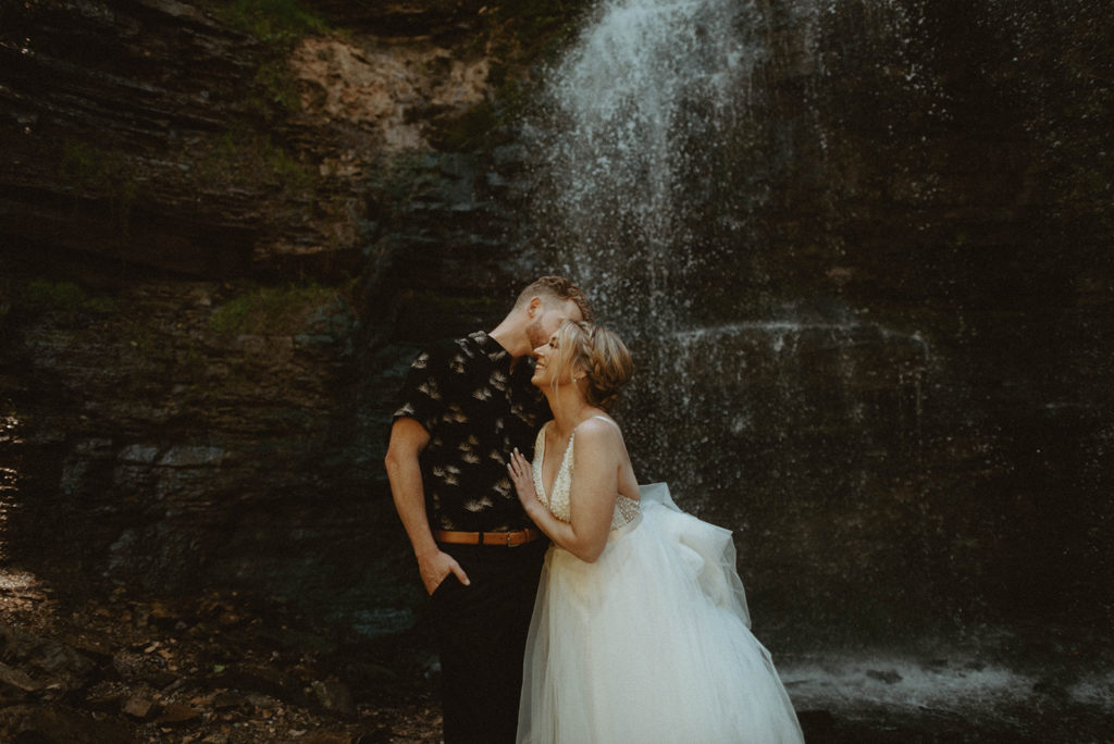 bride and groom in front of waterfall