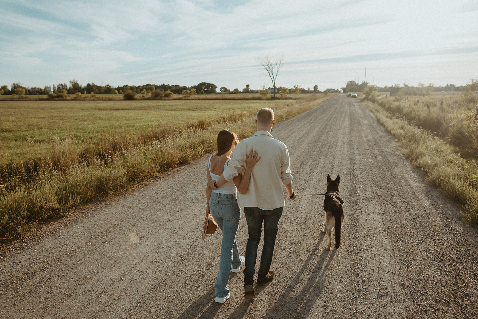 man and woman walking down sunny road with dog