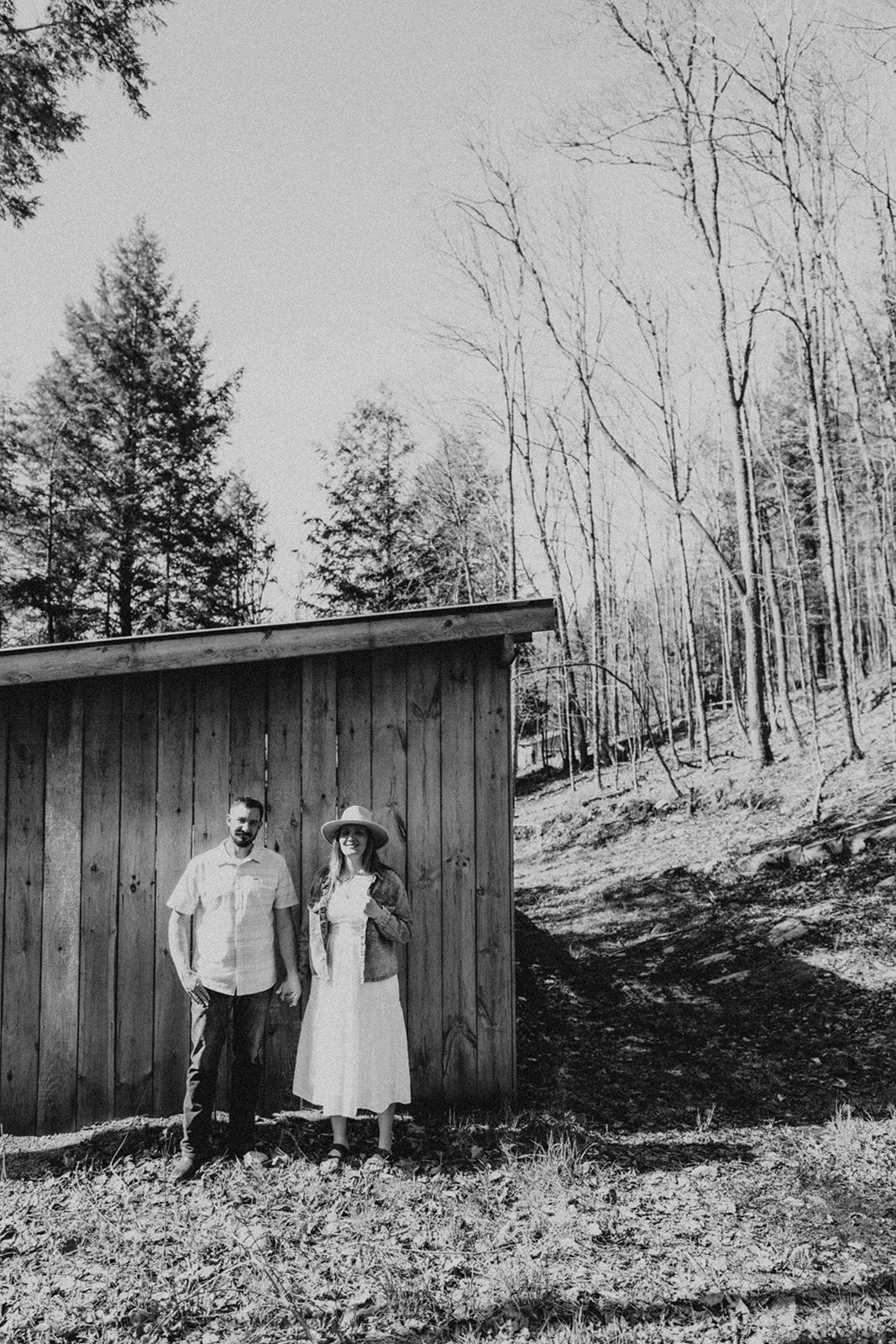 couple standing in forest in front of wooden shed