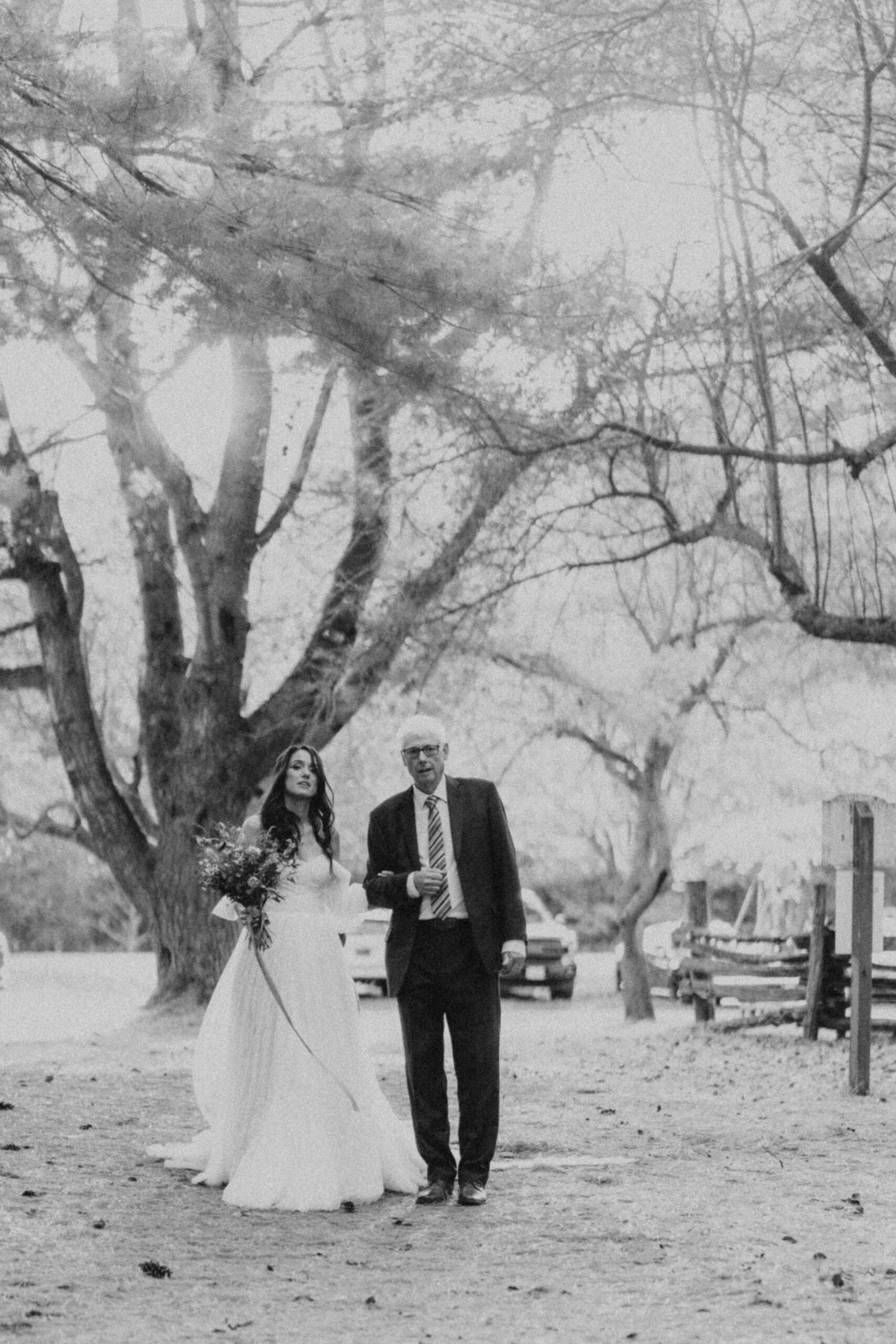father walking bride down the aisle for an outdoor ceremony in the woods